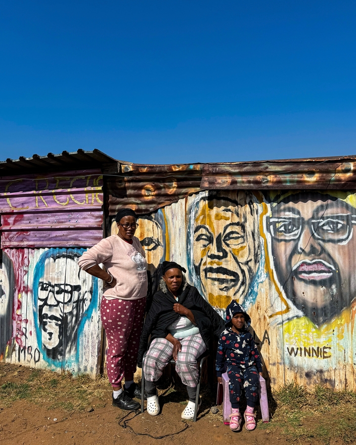 Two women posing in front of a corrugated metal artwork wall.