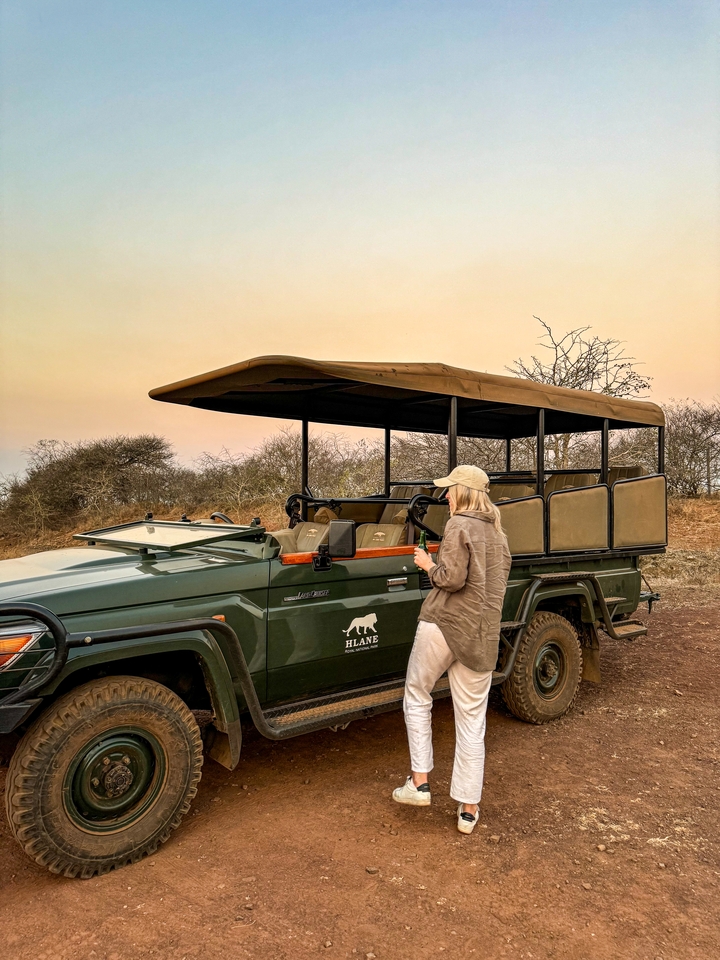 Person standing next to a safari vehicle at sunset.
