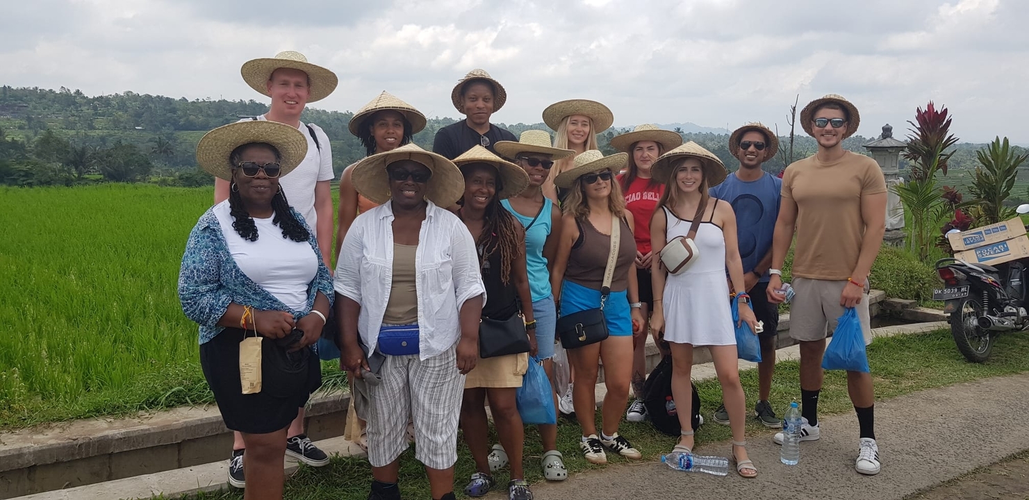 Group of tourists posing in front of a rice field, wearing straw hats.