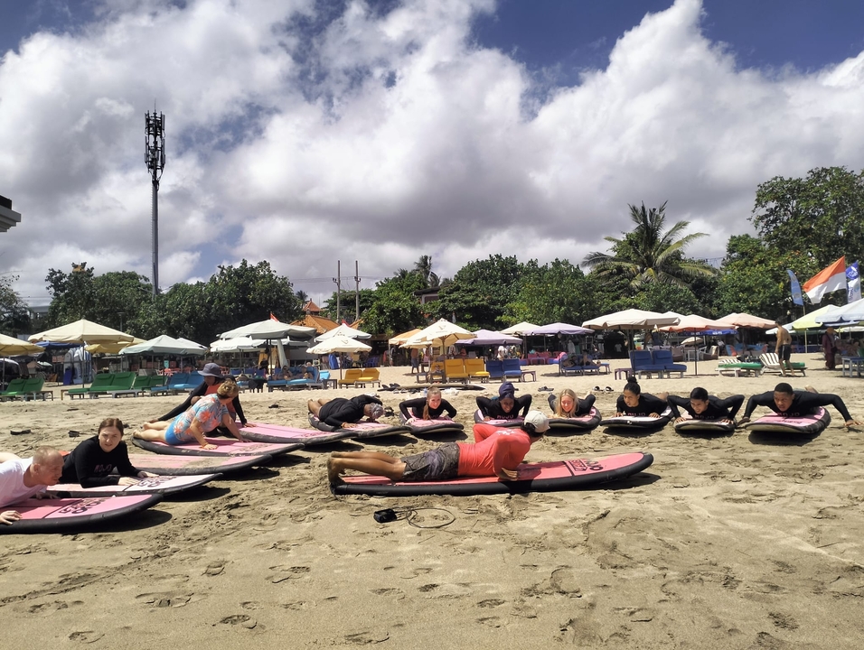 Surfing lesson on a sandy beach with people lying on surfboards.