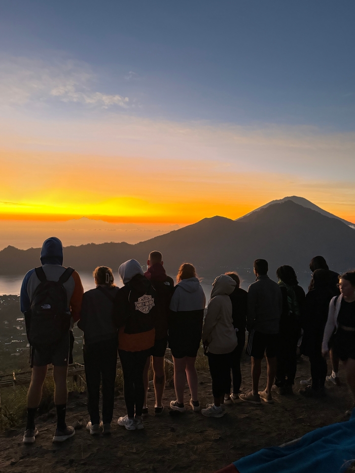 People gathered watching a scenic sunrise over mountains.