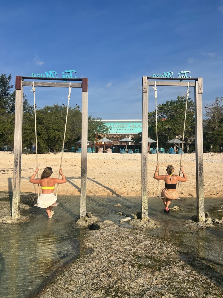Two women sitting on swings facing a beachfront villa.