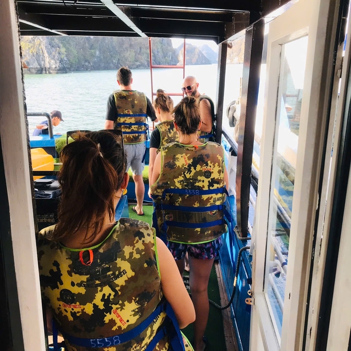 Des gens portant des gilets de sauvetage sur un bateau avec de l'eau en arrière-plan.