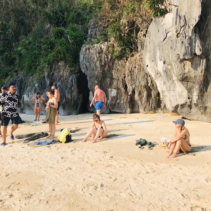 Des touristes sur une plage de sable avec des falaises calcaires.