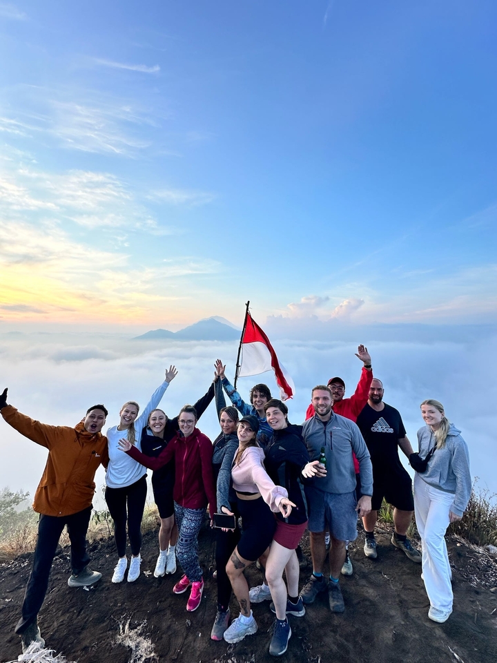 Group of people on a mountain with an Indonesian flag, surrounded by clouds.