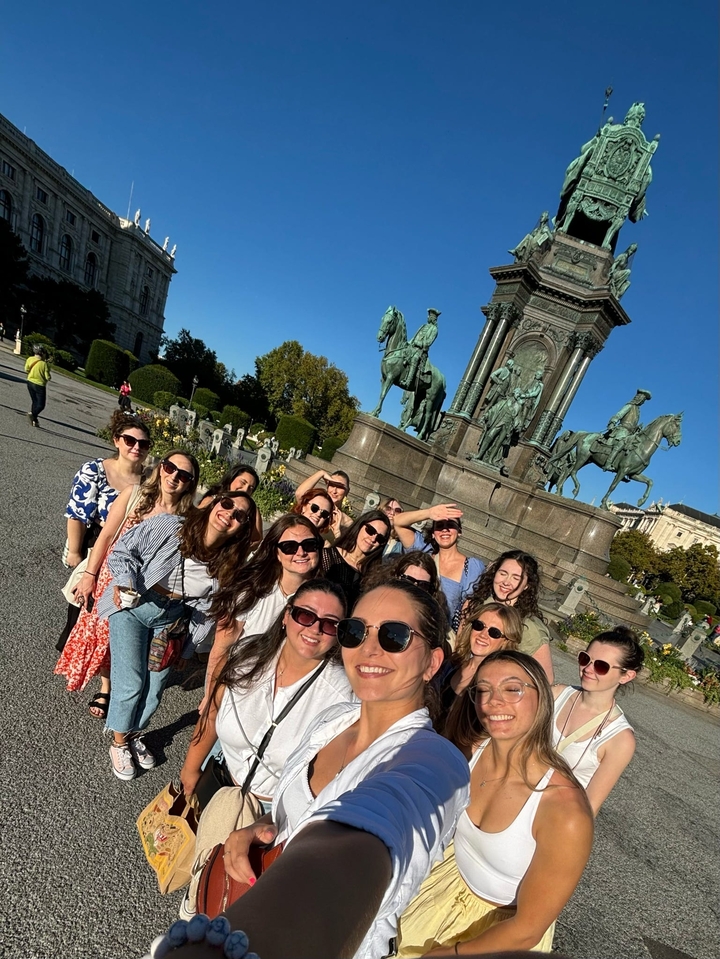 Large group posing by a statue in a city square.