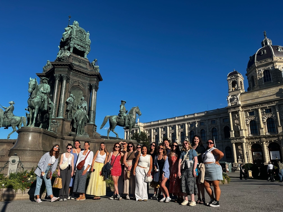 Large group posing by a statue in a city square.
