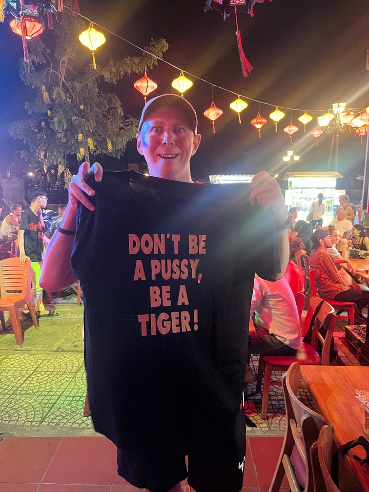 Eine Person, die ein T-Shirt mit Text in einer überfüllten Außenumgebung hält.