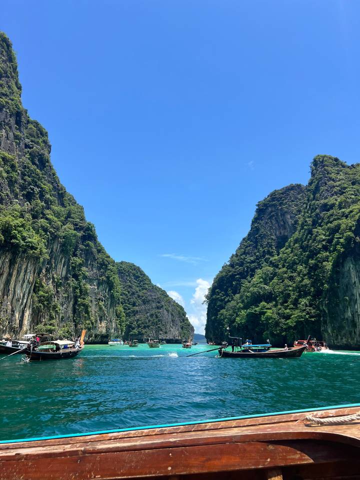 Sheer limestone cliffs draped in jungle tower toward a bright blue sky over a narrow waterway.