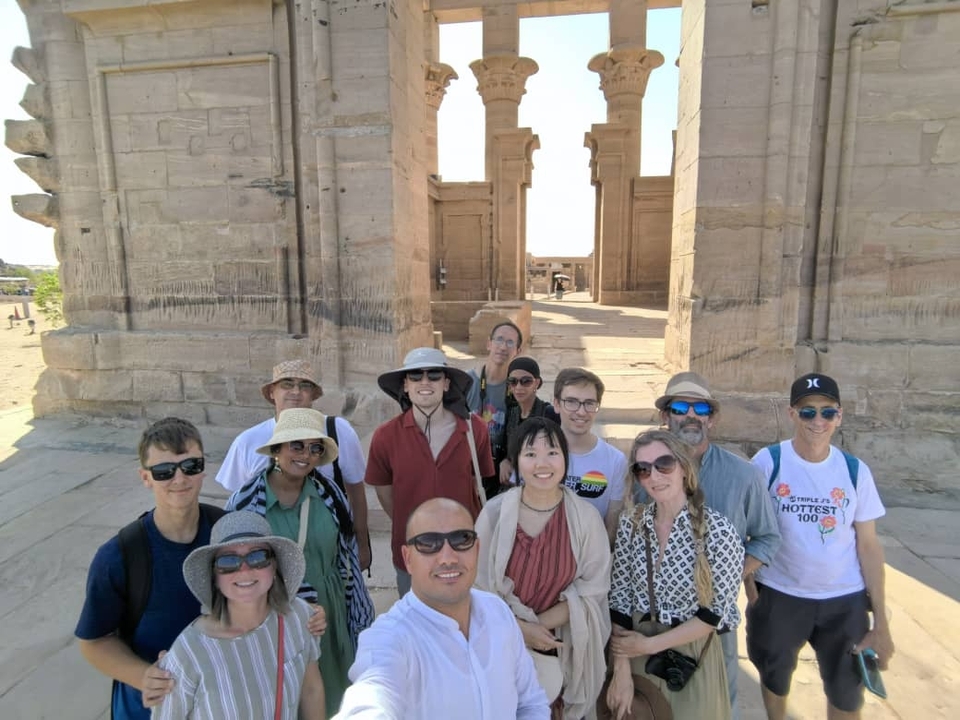 A group of tourists posing in front of ancient stone pillars during the day.