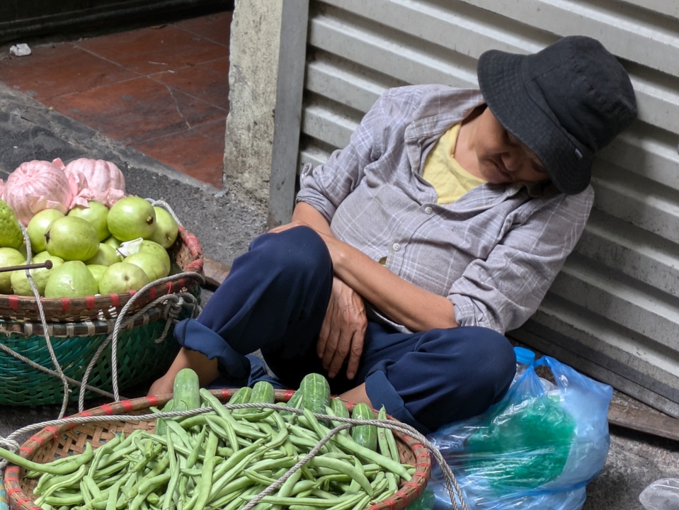 Market scene with a vendor napping amidst baskets of fruit.