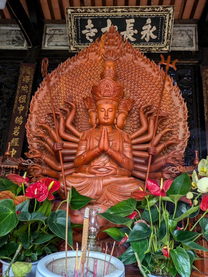 Intricately carved statue of a multi-armed deity with colorful flowers.