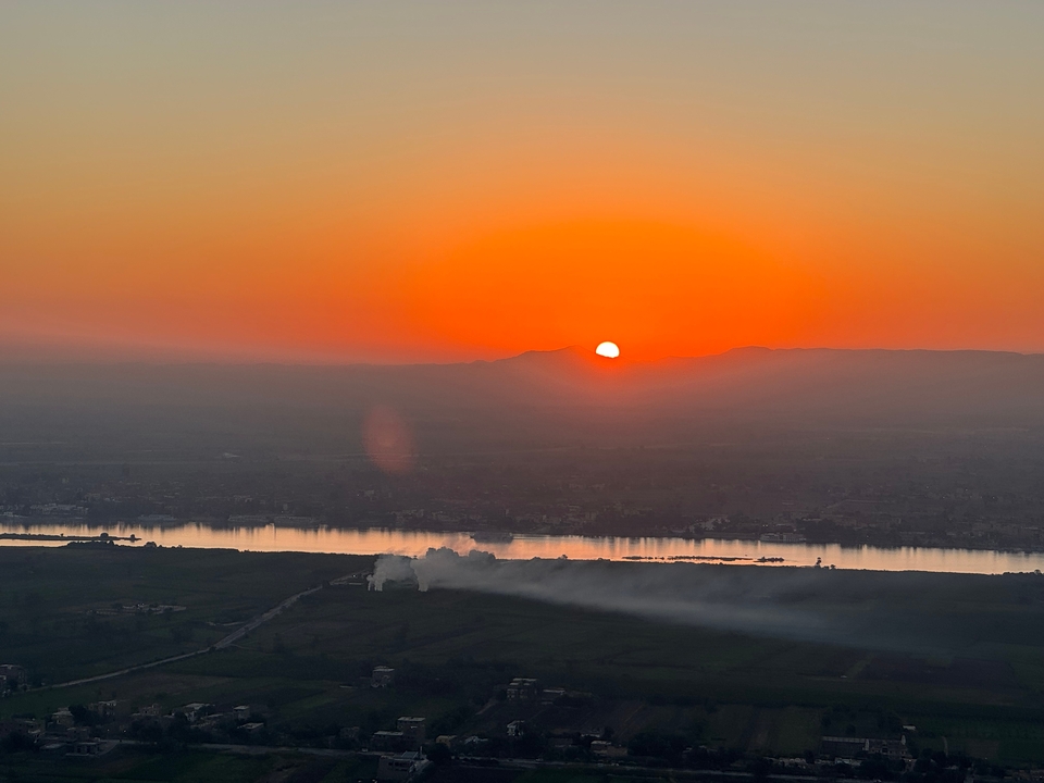 Sunset over a river with smoke rising from a field