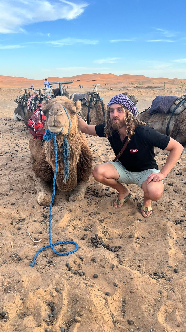 Homme posant avec un chameau dans un désert.
