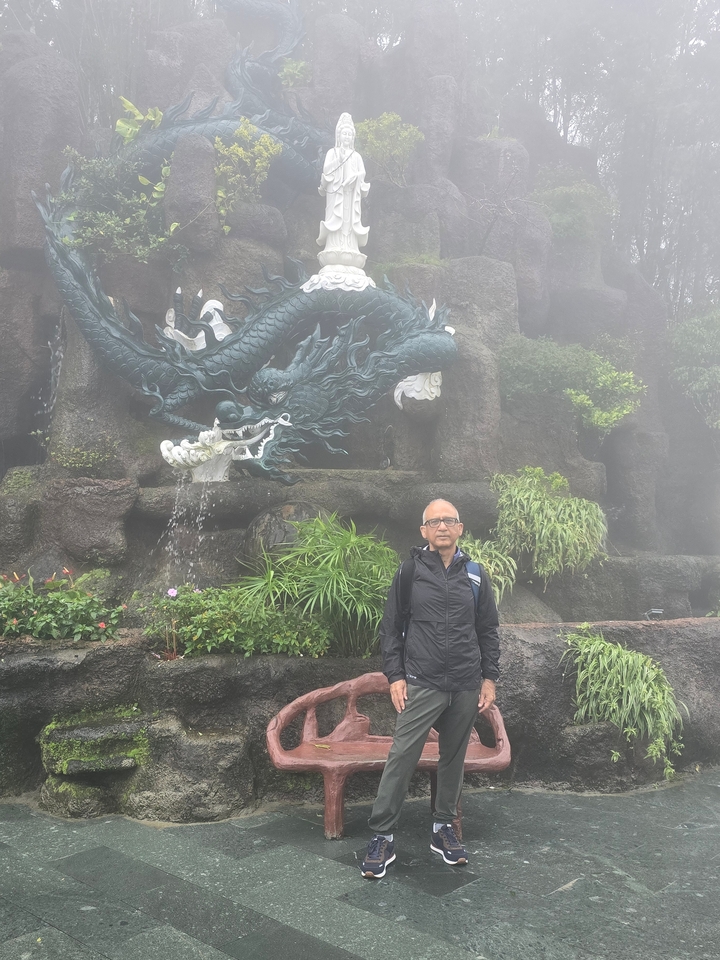Man posing in front of a dragon statue surrounded by mist.