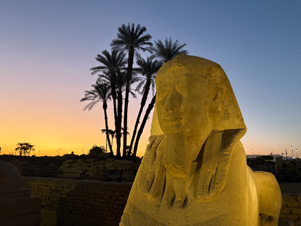 Statue au coucher du soleil avec des palmiers en arrière-plan.