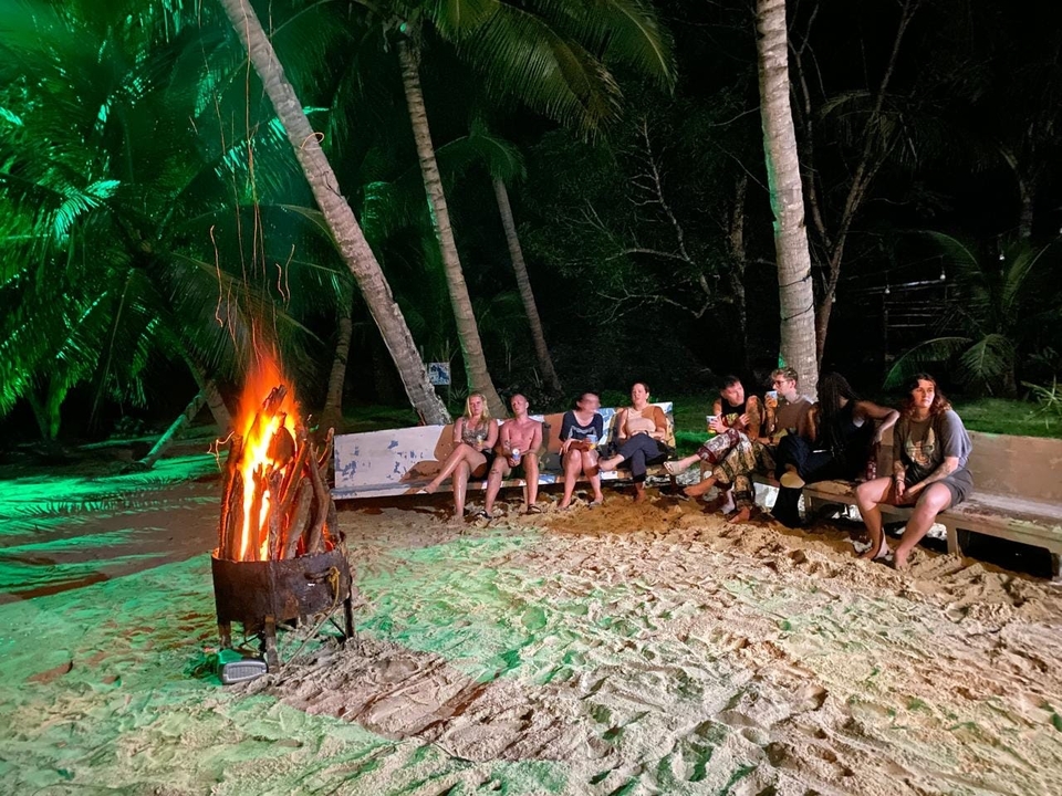Groupe de personnes assises autour d'un feu de camp sur la plage.