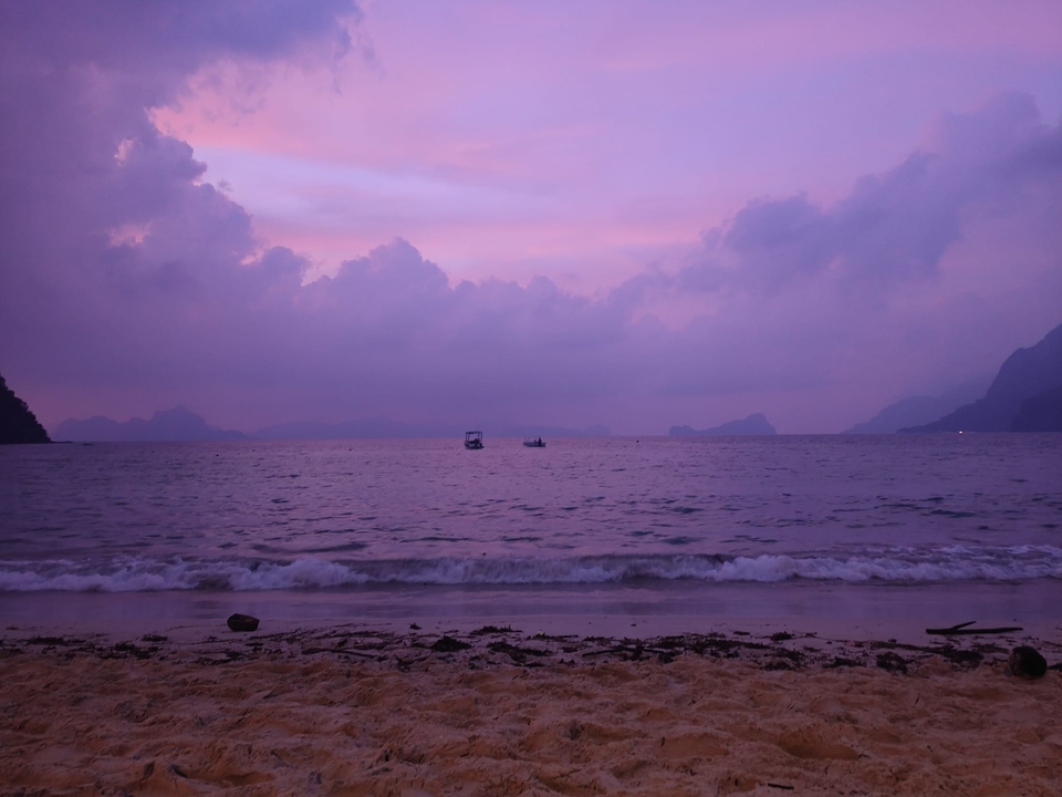 Plage au coucher du soleil avec des bateaux à l'horizon.