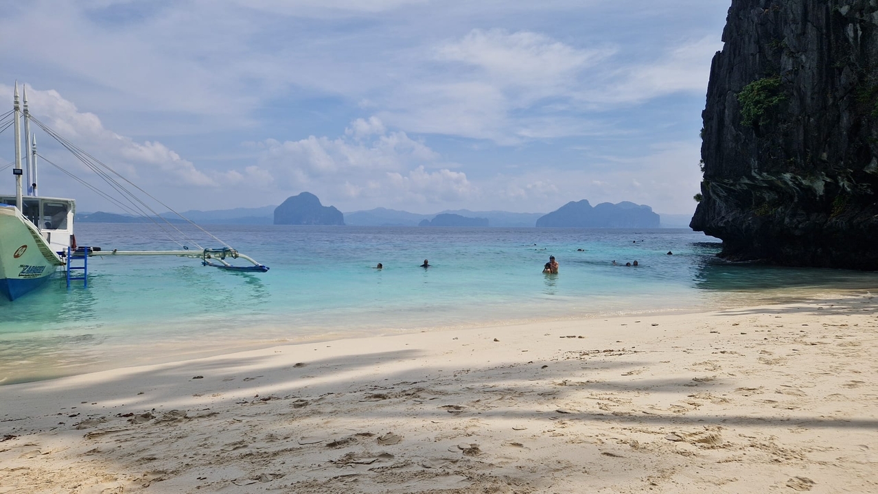 Plage d'eau claire avec des nageurs et un bateau.
