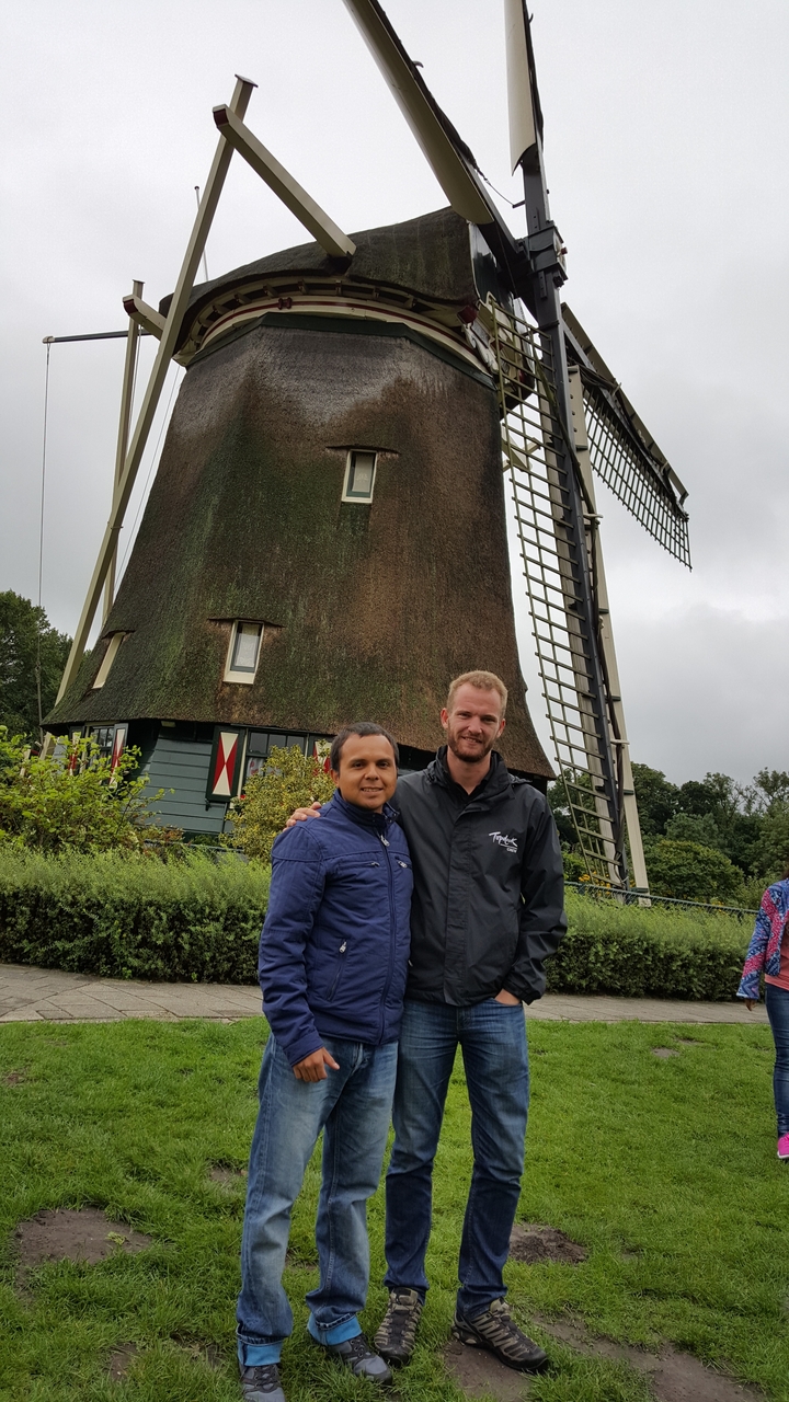 Two men posing in front of a traditional windmill.