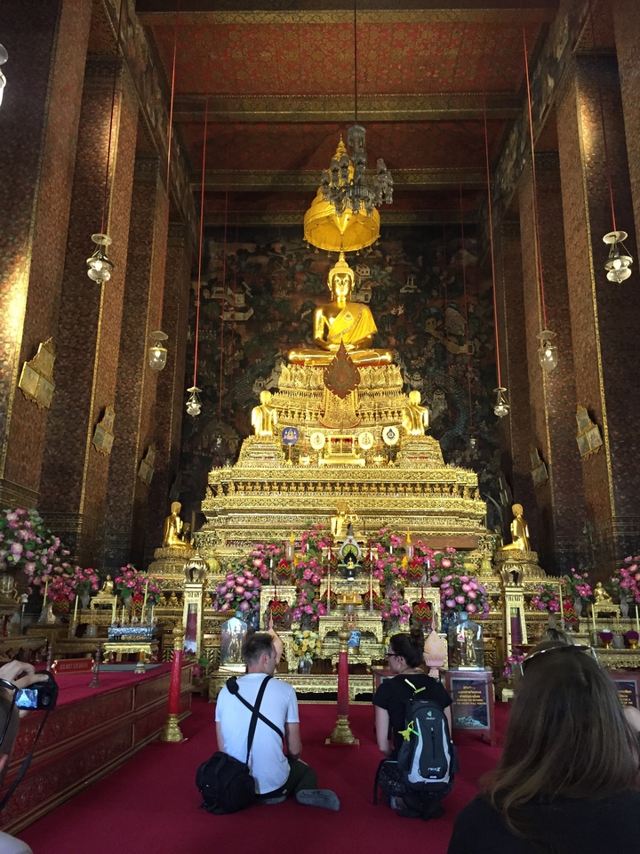 Magnificent golden Buddha seated atop an elaborate tiered altar inside a richly decorated temple.