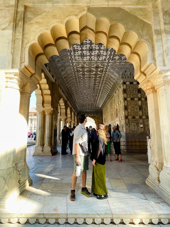 Des personnes marchant dans un couloir décoré de manière complexe avec des arches détaillées.