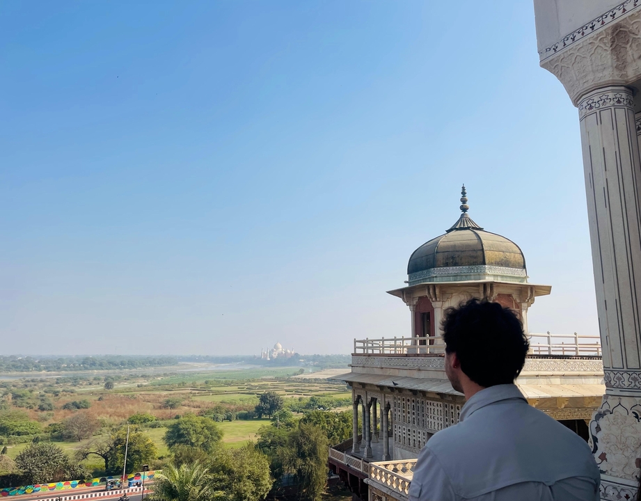 Un homme observant une vue lointaine du Taj Mahal depuis un bâtiment historique.