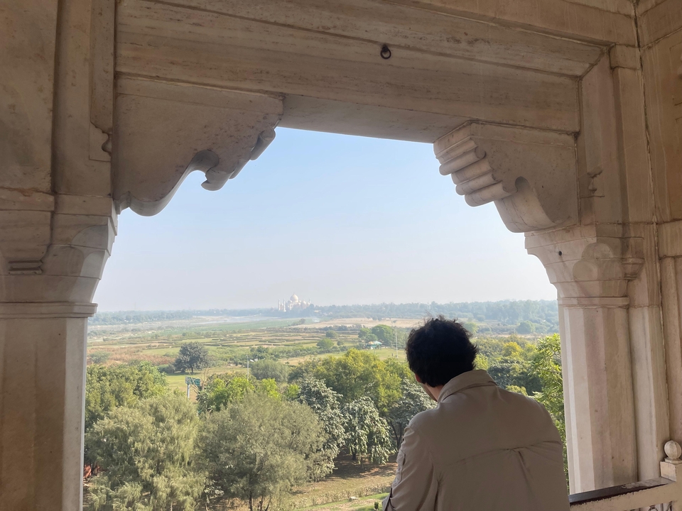 Une personne regardant vers le Taj Mahal, la vue partiellement obstruée par une structure en pierre.