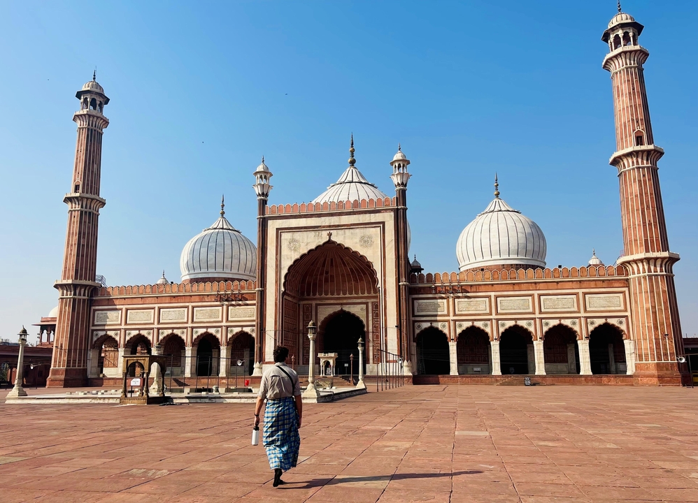 Une personne debout devant une structure de mosquée majestueuse avec un ciel bleu.