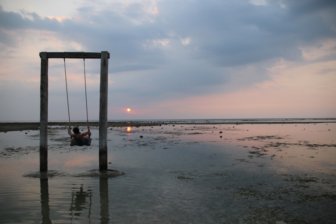 Person on a swing over water at sunset.