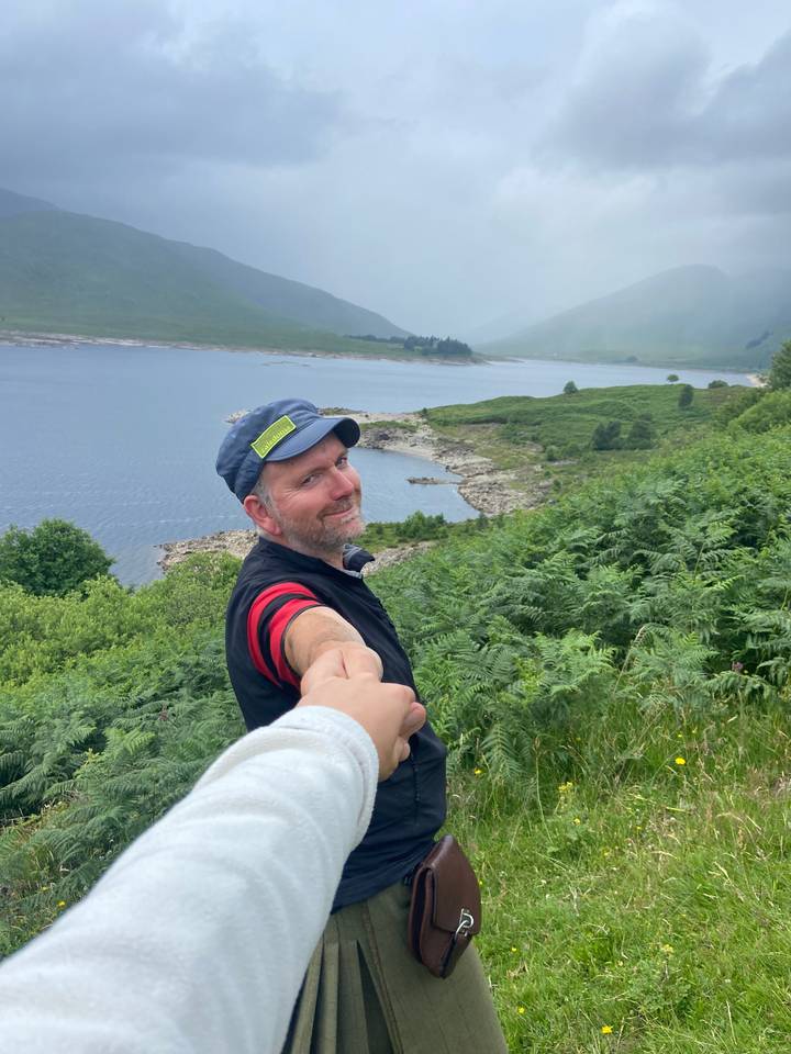 Person holding hands in a green landscape by a lake.