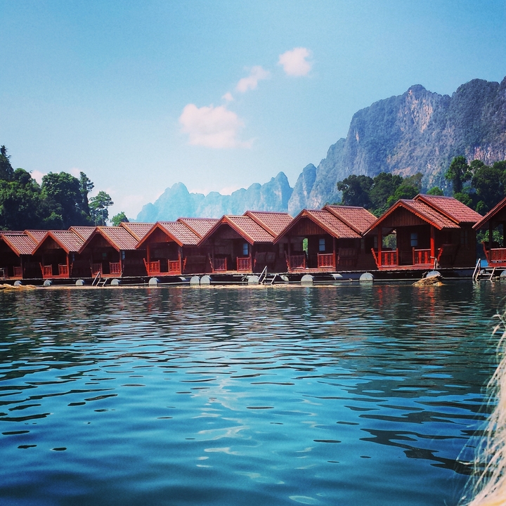 Row of wooden cabins on water with mountains in the background.