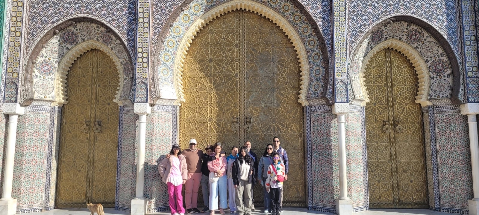 A group of people posing in front of large, ornate golden doors with mosaic decorations.