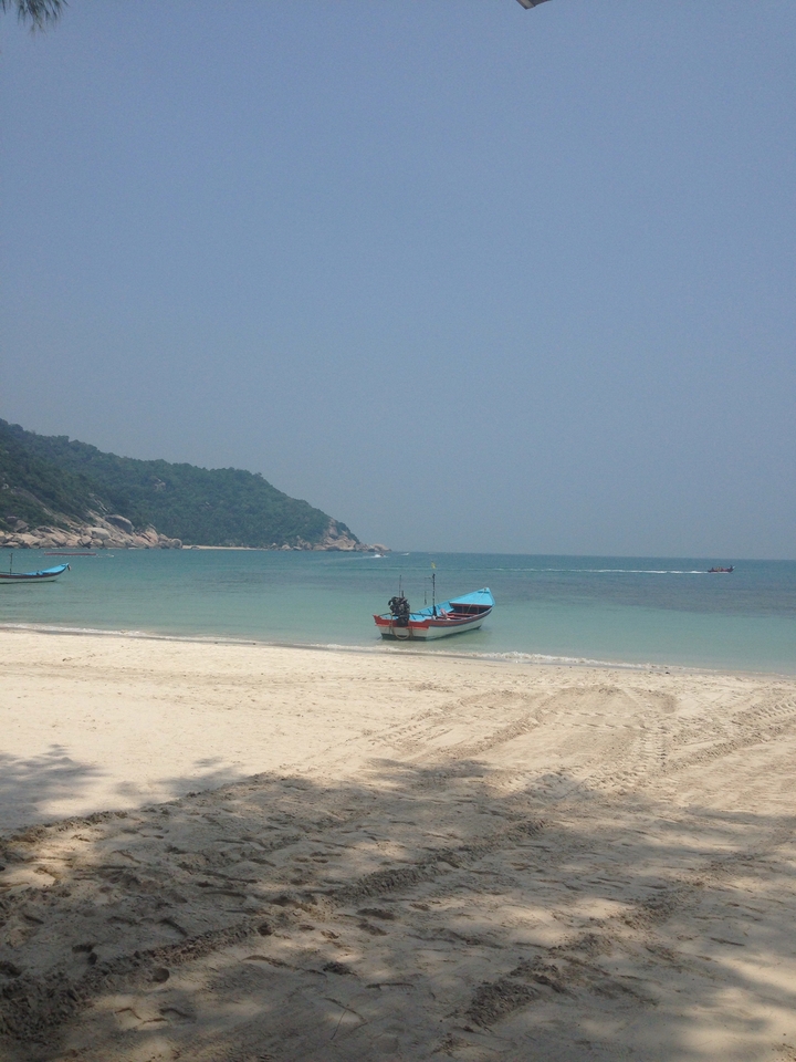 Beach scene with a small boat and hills in the background.