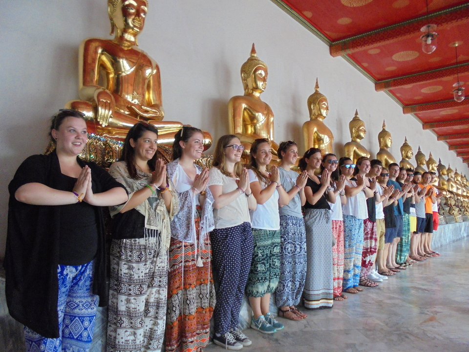 Group of people posing in front of golden Buddha statues.