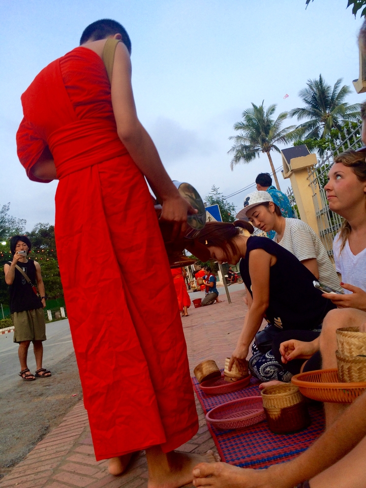 People sitting with monks during an outdoor ceremony.