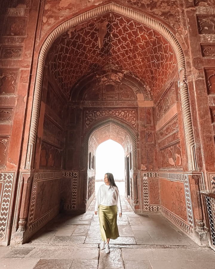 Woman standing in an ornate archway with intricate carvings, bright light in background.