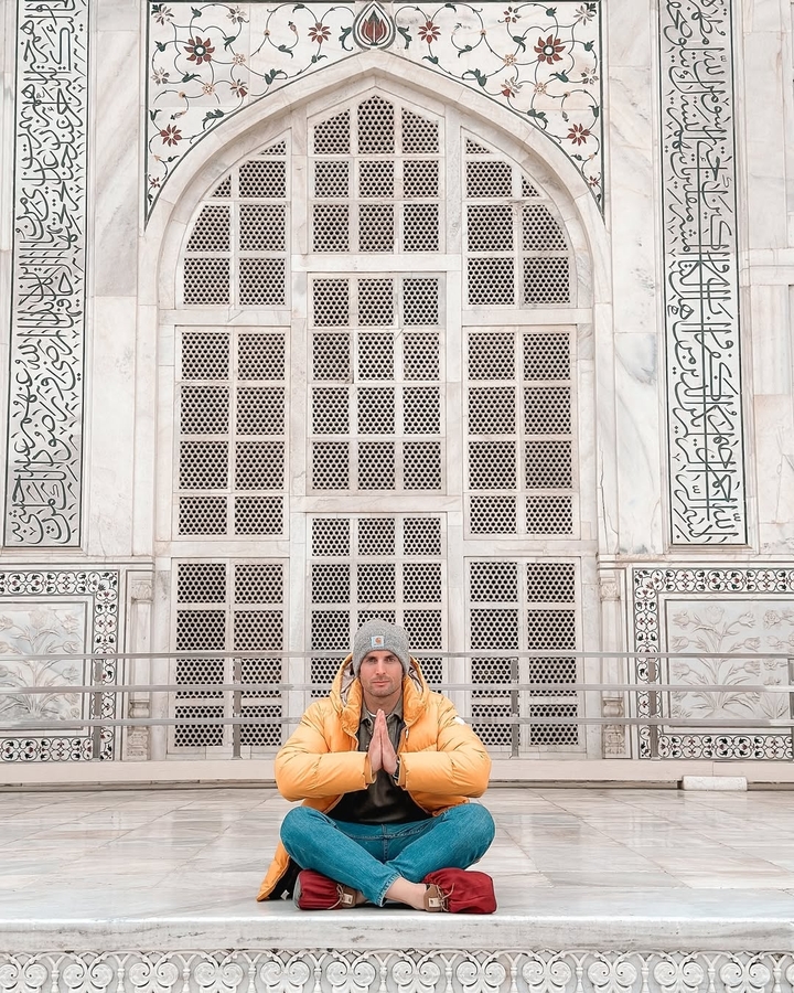 Man sitting in front of intricately patterned wall with calligraphy.