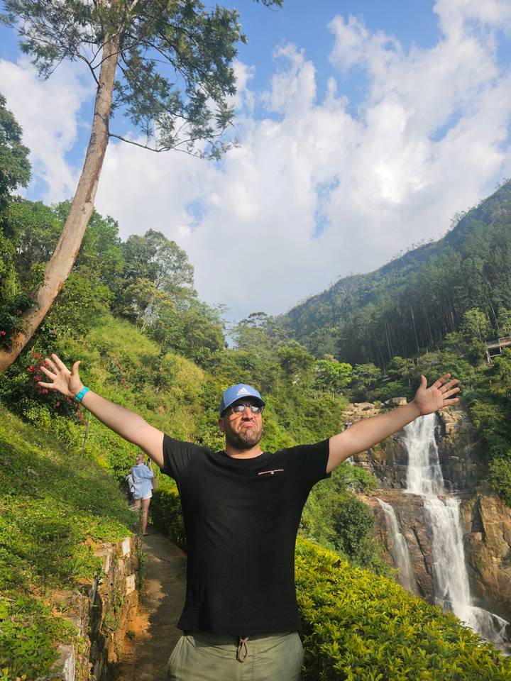 Personne posant devant une cascade dans une forêt luxuriante.