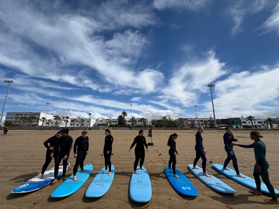 Group of people in wetsuits standing on a beach with surfboards.