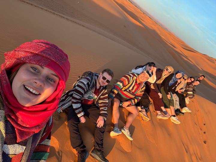 Group of people sitting on a sand dune at sunset.