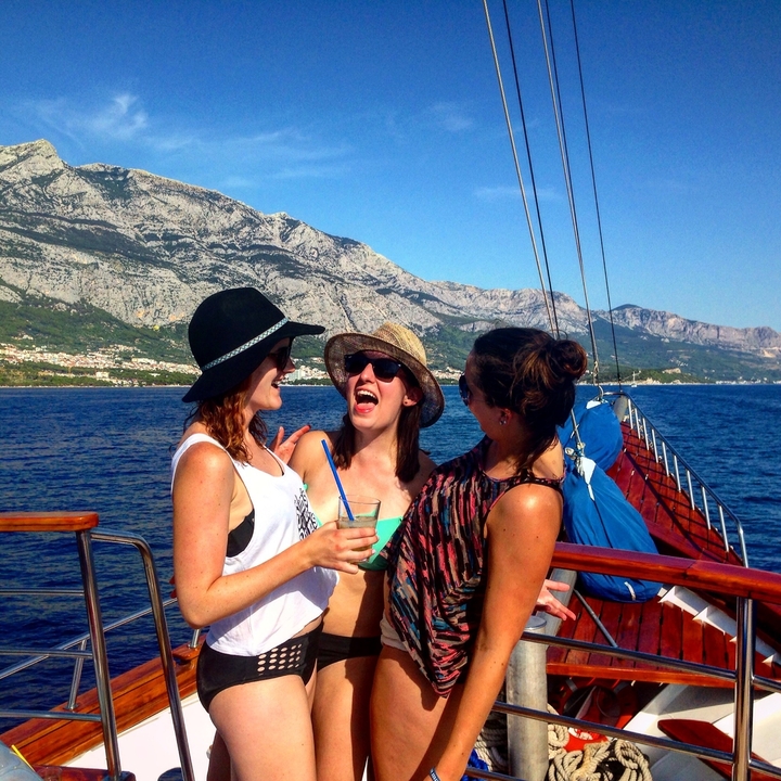 Group of friends laughing on a boat with mountainous background.