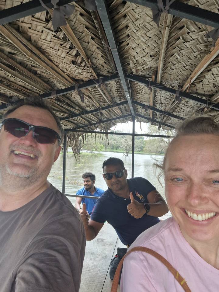 Trois personnes sur un bateau en bois avec un toit de chaume sur une voie navigable.