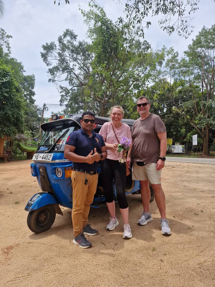 Trois personnes debout à côté d'un tuk-tuk, souriantes.