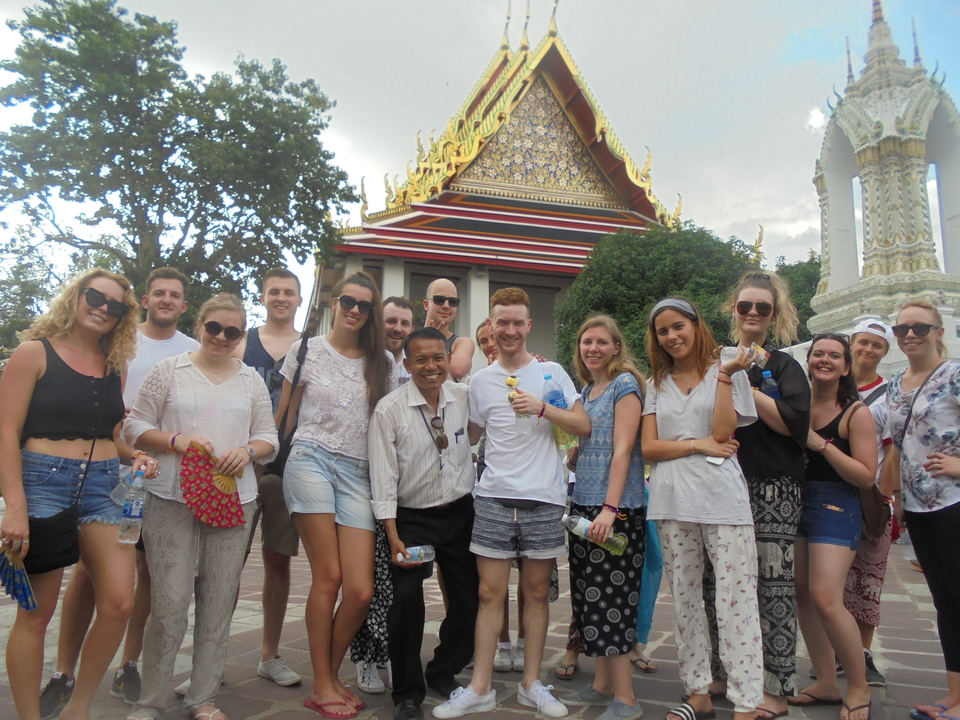 Tour group posing in front of an ornate Bangkok temple with golden roof details