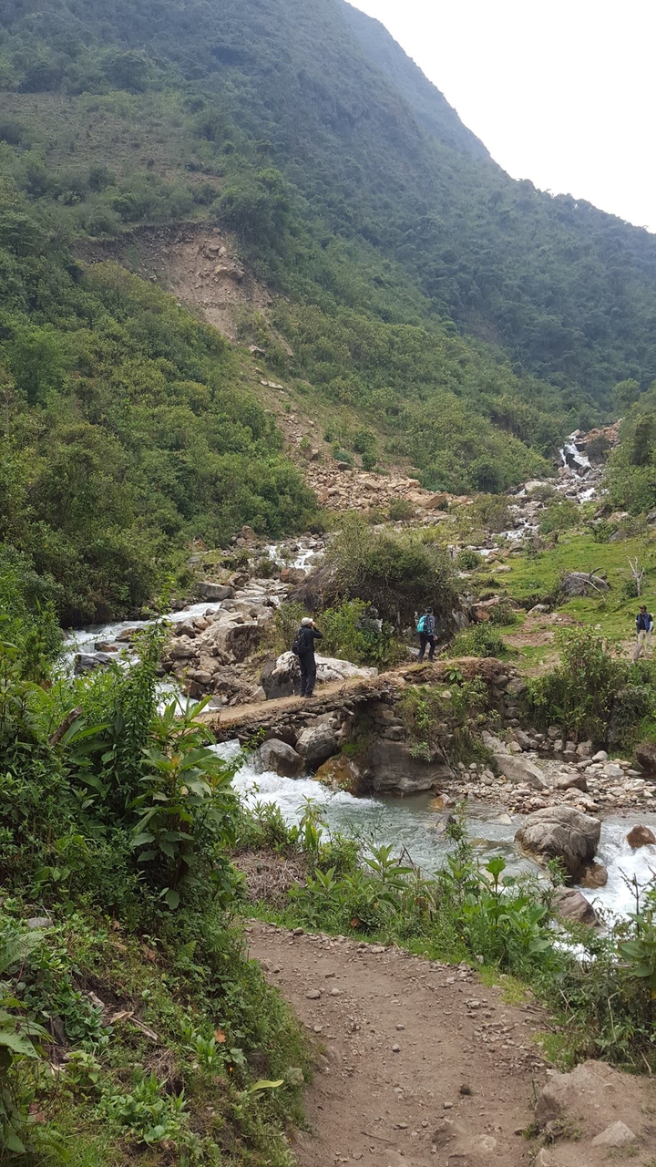 People crossing a stream on a wooden bridge.