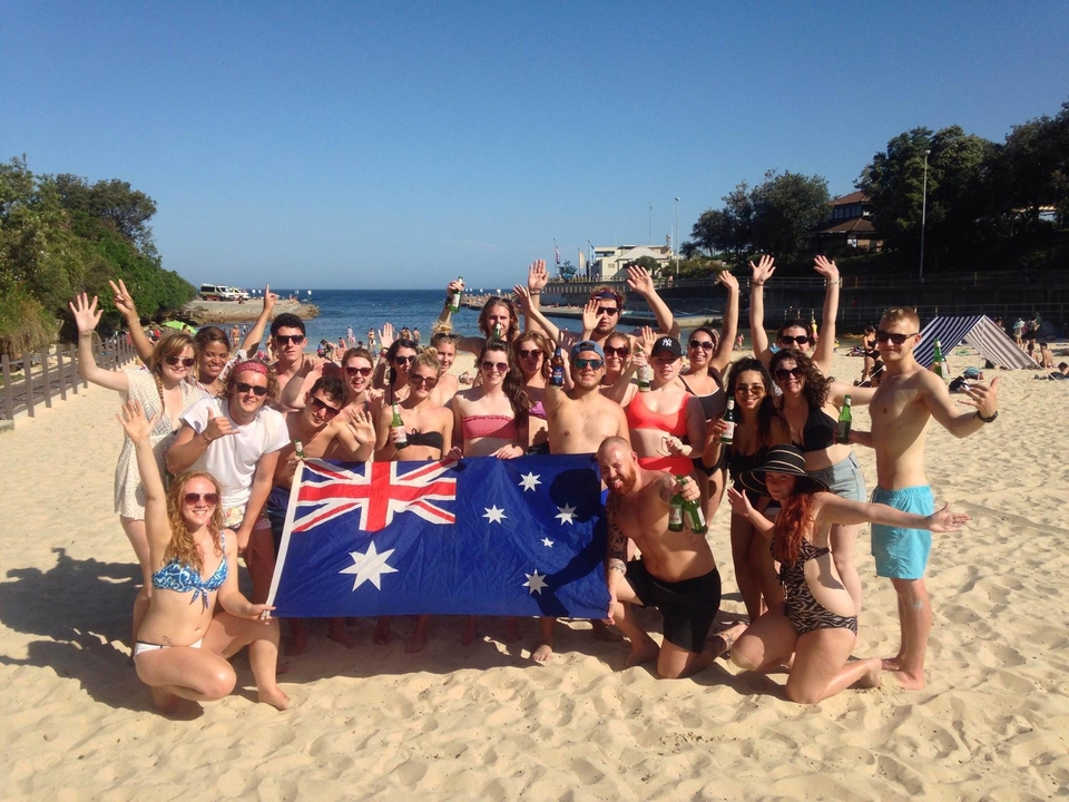 Group posing with an Australian flag on a beach.