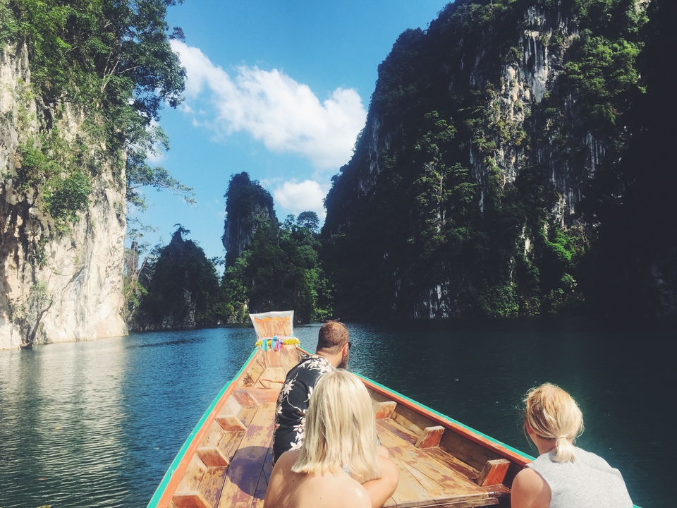 People on a boat heading towards scenic limestone cliffs.