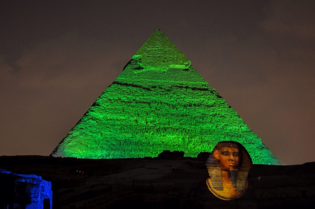 Illuminated pyramid at night with a Sphinx in the foreground.