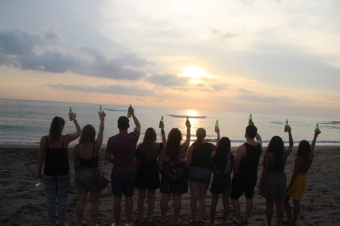 Group of people raising bottles on the beach during sunset.